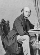 portrait of Francis Gallton seated at a writing desk